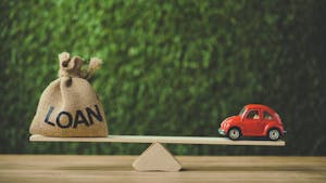 Red miniature car and money bag with word loan balancing on seesaw on green background
